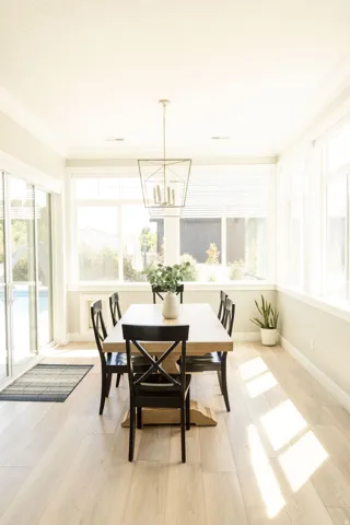 Dining area featuring wood-finish flooring, a contemporary chandelier, abundant natural light, crown molding, and sliding glass doors