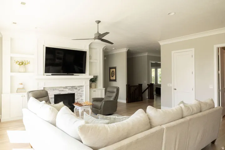 Living area featuring a fireplace with stacked stone surround, built-in shelving, crown molding, and wood-finish flooring