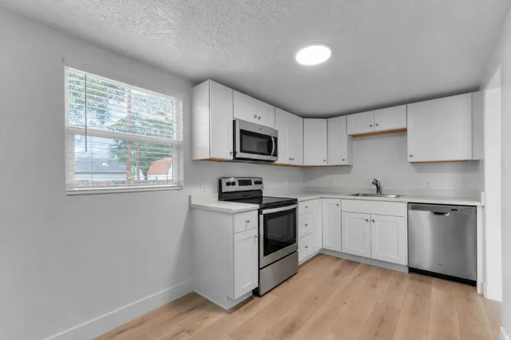 Appliances are virtually staged (actual stainless steel appliances are included). Kitchen featuring white cabinetry, stainless steel appliances, light-toned wood-finish flooring, a window, and a recessed ceiling light