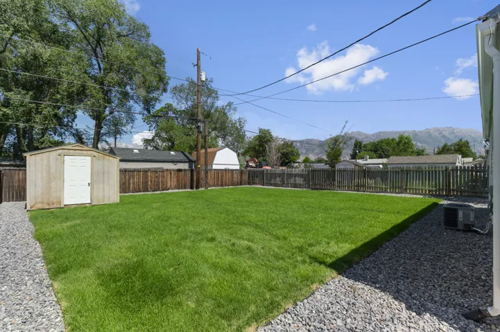 Expansive lawn area, gravel hardscaping, wood-paneled storage shed, slatted wood fencing, and distant mountain scenery