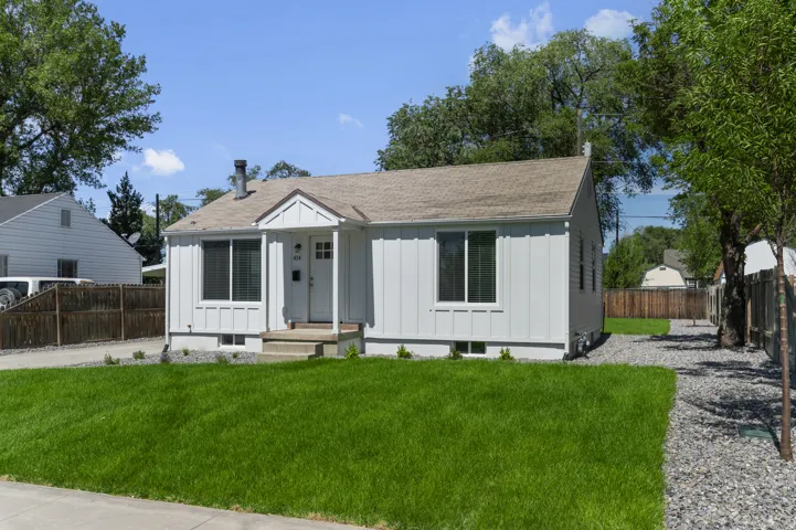White exterior siding with a covered entry, established landscaping, gravel pathway, and a brown shingle roof