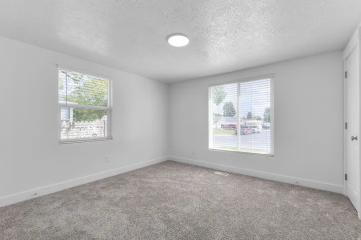 Recessed ceiling light fixture, two windows with horizontal blinds, neutral wall paint, and gray carpet flooring