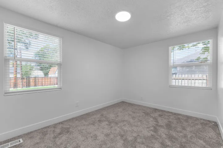 Recessed circular lighting fixture, two windows with blinds, gray carpet flooring, and white painted walls