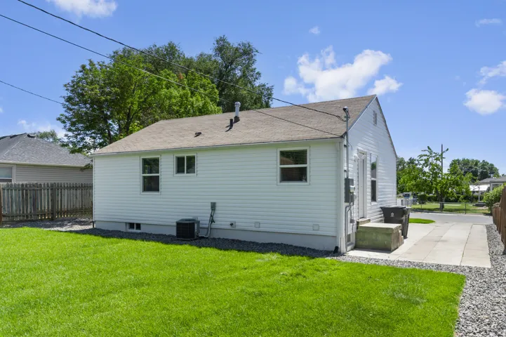 Expansive grassy yard with a concrete patio, gravel border, and white siding exterior