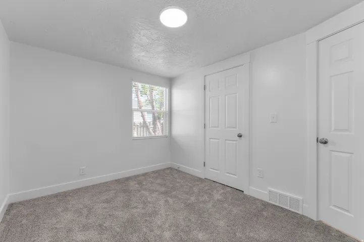 Plush gray carpeting, white painted walls, and a single window with horizontal blinds