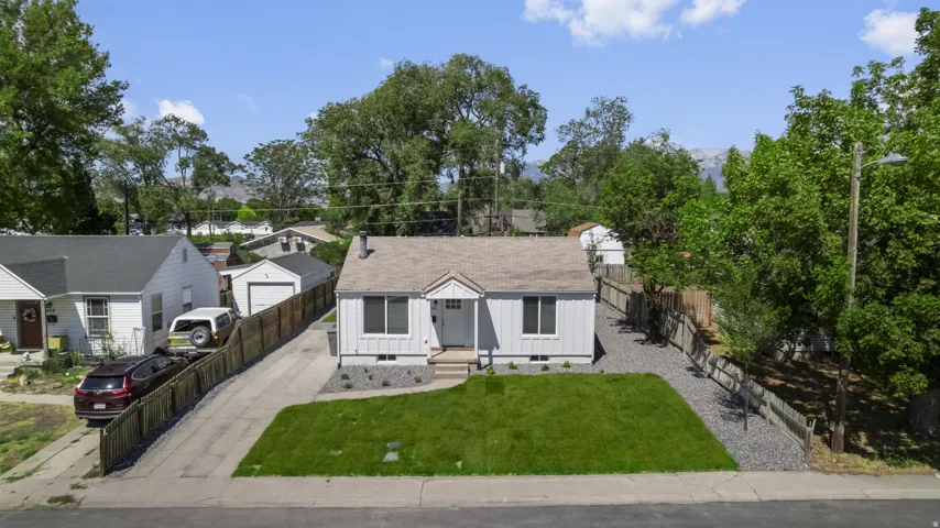 White exterior with a gable roof, front lawn, gravel landscaping, and a fenced perimeter