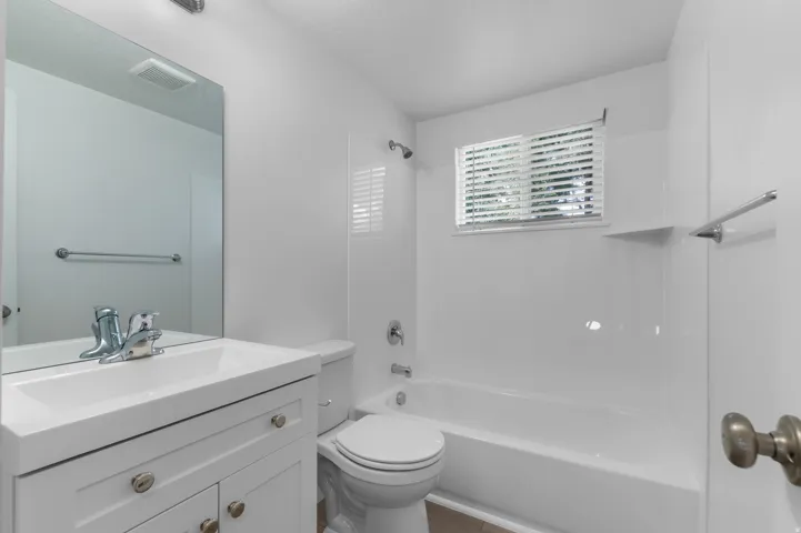 Bathroom featuring a white vanity with integrated sink, chrome faucet, wall-mounted mirror, and a combination shower/bathtub with white surround