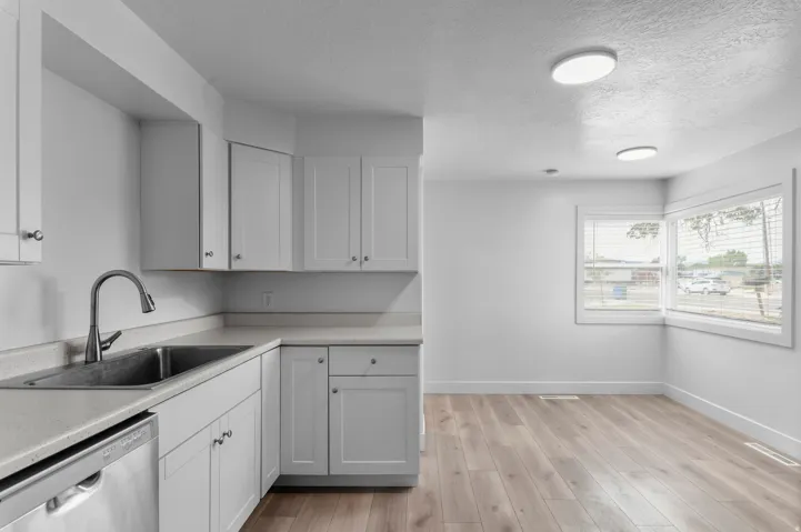 Recessed ceiling lighting, wood-finish flooring, white cabinetry, stainless steel sink, and a built-in dishwasher
