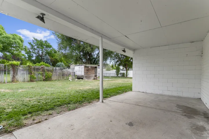 Covered patio with concrete flooring, white block wall, and exposed white ceiling beams