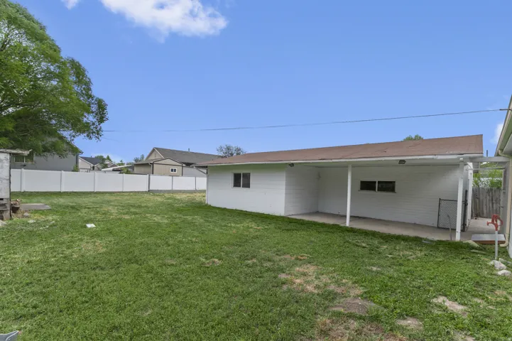Expansive backyard featuring a covered patio, a detached structure, and a white privacy fence