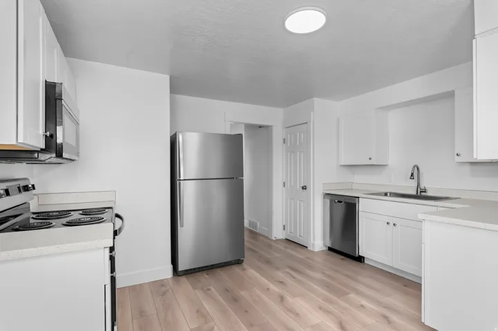 Kitchen featuring white cabinetry, light wood-finish flooring, stainless steel appliances, and solid surface countertops