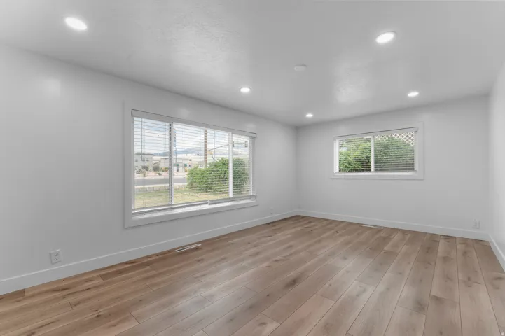 Recessed ceiling lighting, multiple windows with blinds, wood-finish flooring, and crisp white walls