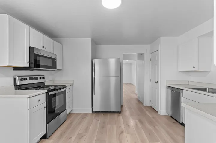 Modern kitchen featuring stainless steel appliances, white cabinetry, light countertops, and wood-finish flooring