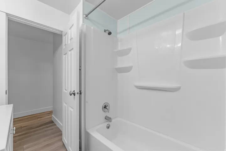 White fiberglass bathtub and shower surround with integrated shelving and a chrome shower fixture