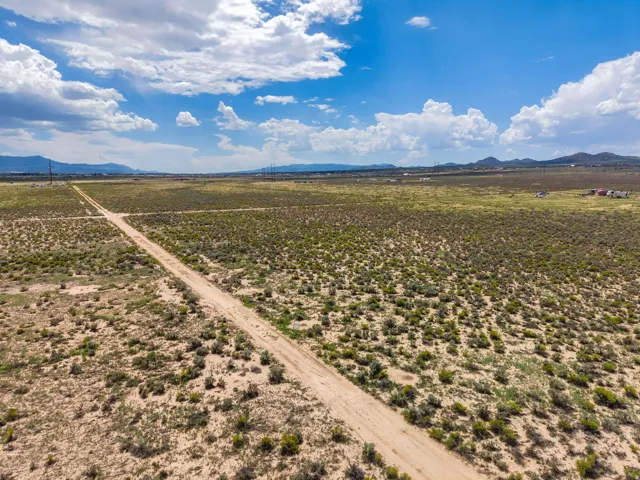 Expansive undeveloped land featuring a dirt road and distant mountains under a blue sky