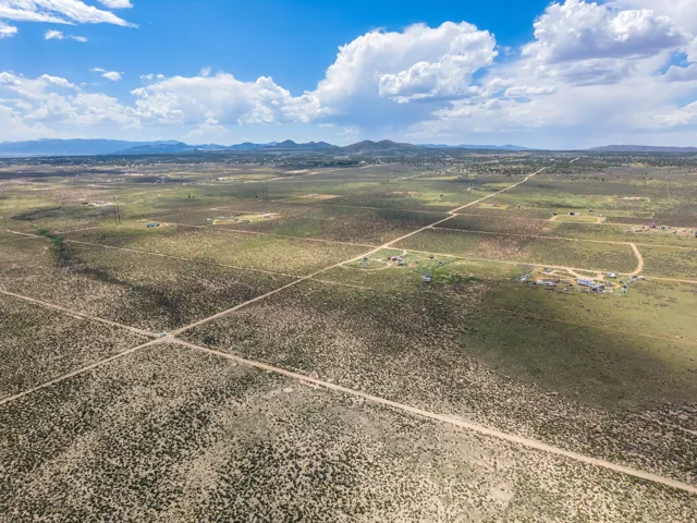 Expansive desert landscape with scattered vegetation, dirt roads, and distant mountains