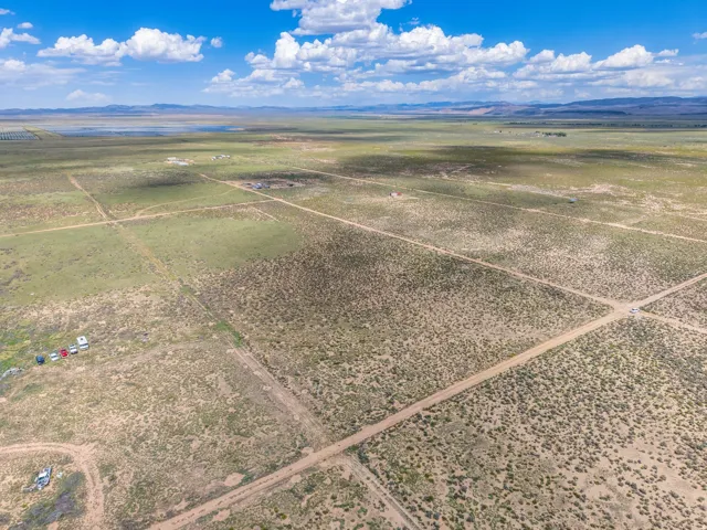 Expansive land parcel with unpaved roads and varied terrain, featuring distant mountains and a prominent water body under a clear sky
