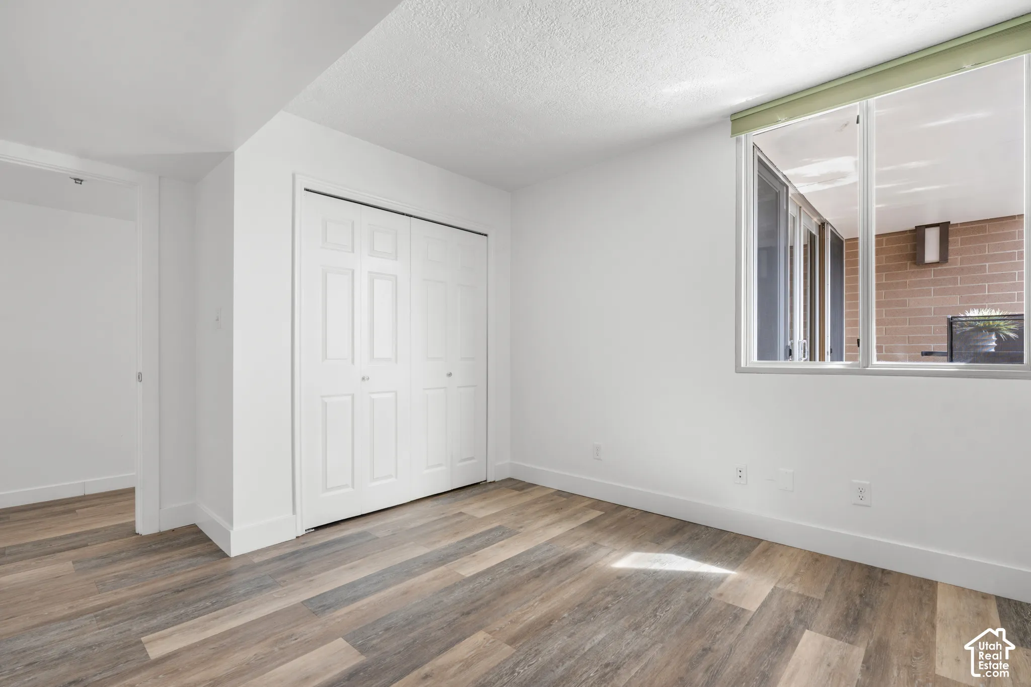 Wood-finish flooring, white bi-fold closet doors, white walls, and a large window with a light-colored roller shade