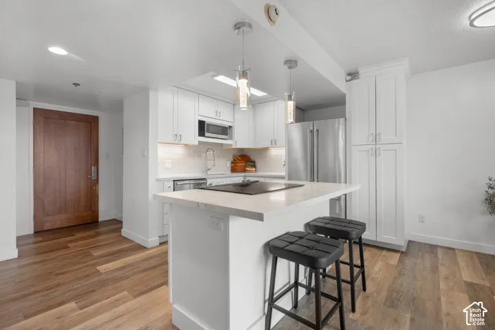 Kitchen featuring a central island with countertop seating, white shaker cabinetry, stainless steel appliances, and wood-finish flooring