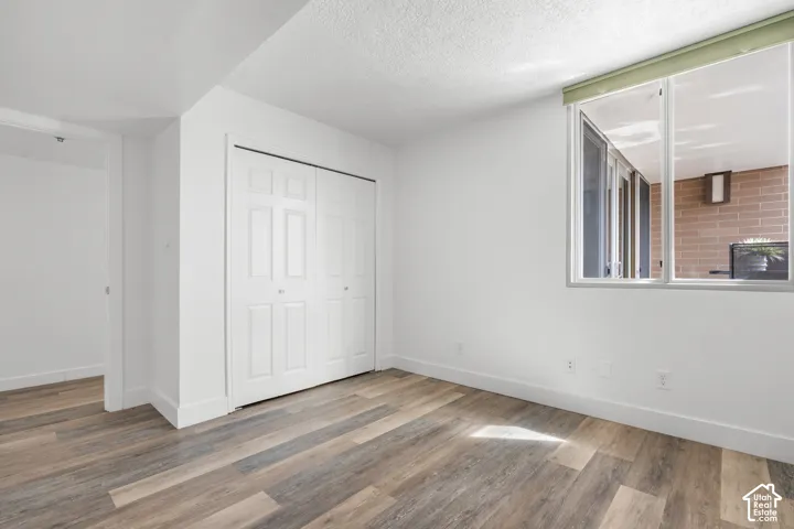 Wood-finish flooring, white bi-fold closet doors, white walls, and a large window with a light-colored roller shade