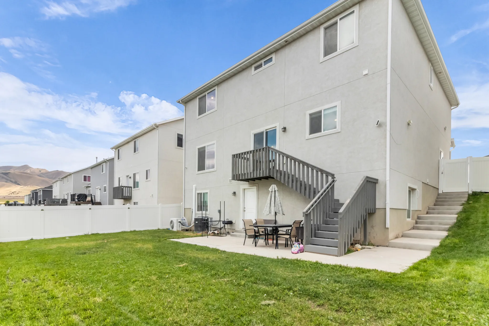 Spacious backyard featuring a concrete patio, exterior staircase, and fenced perimeter