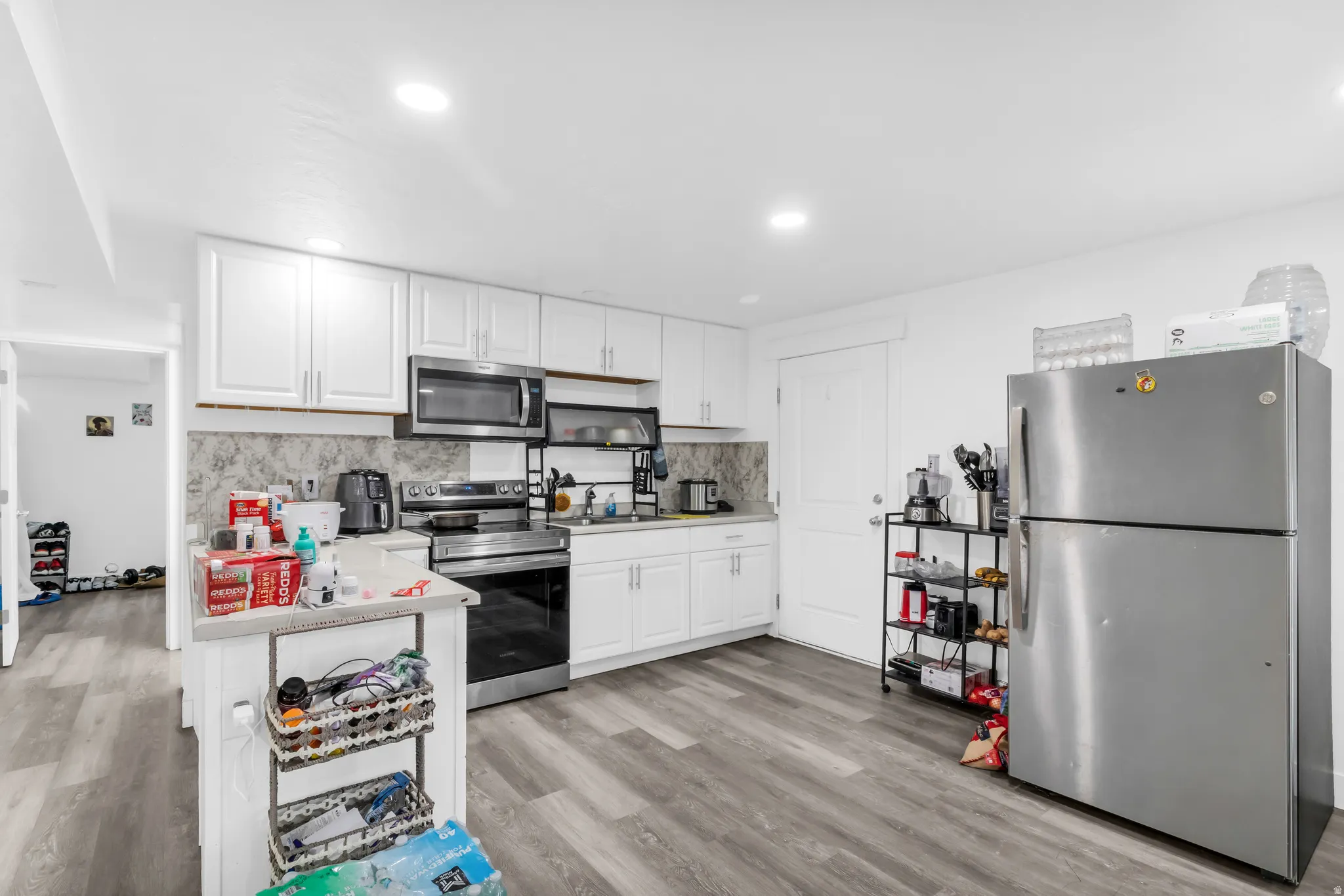 Kitchen featuring stainless steel appliances, white cabinetry, a patterned backsplash, and wood-finish flooring