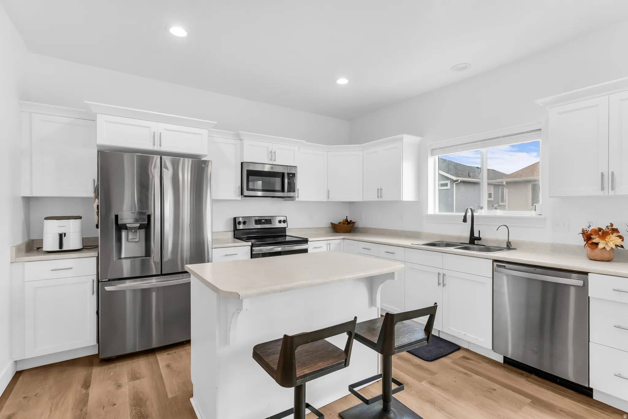 White cabinetry kitchen with stainless steel appliances, light-toned countertops, and wood-finish flooring