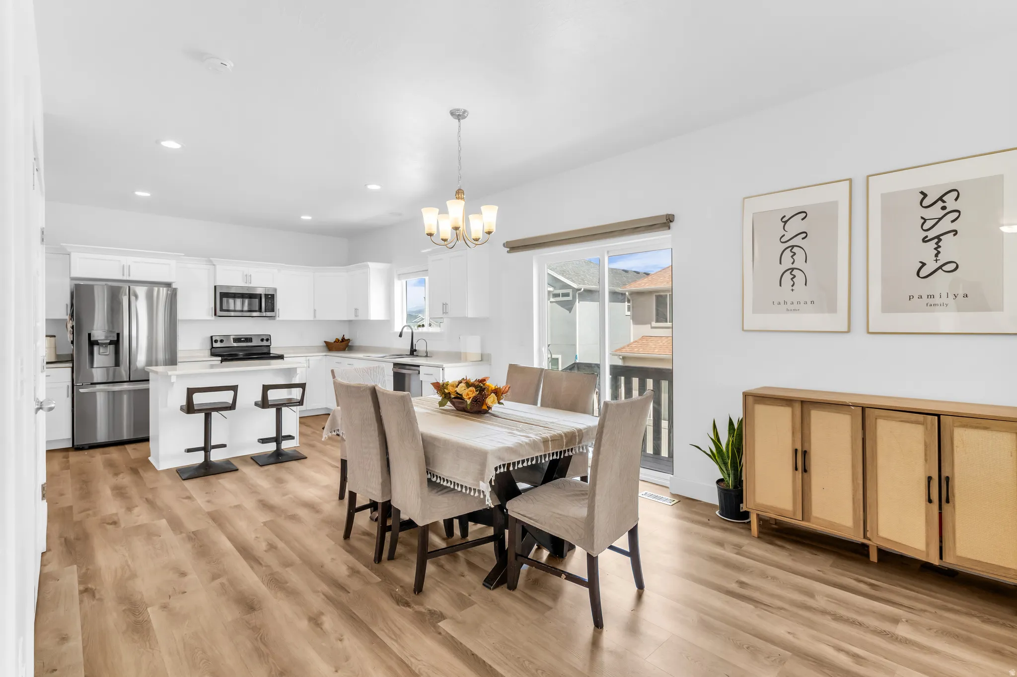 Open-concept living space with wood-finish flooring, white cabinetry, stainless steel appliances, and a sliding glass door