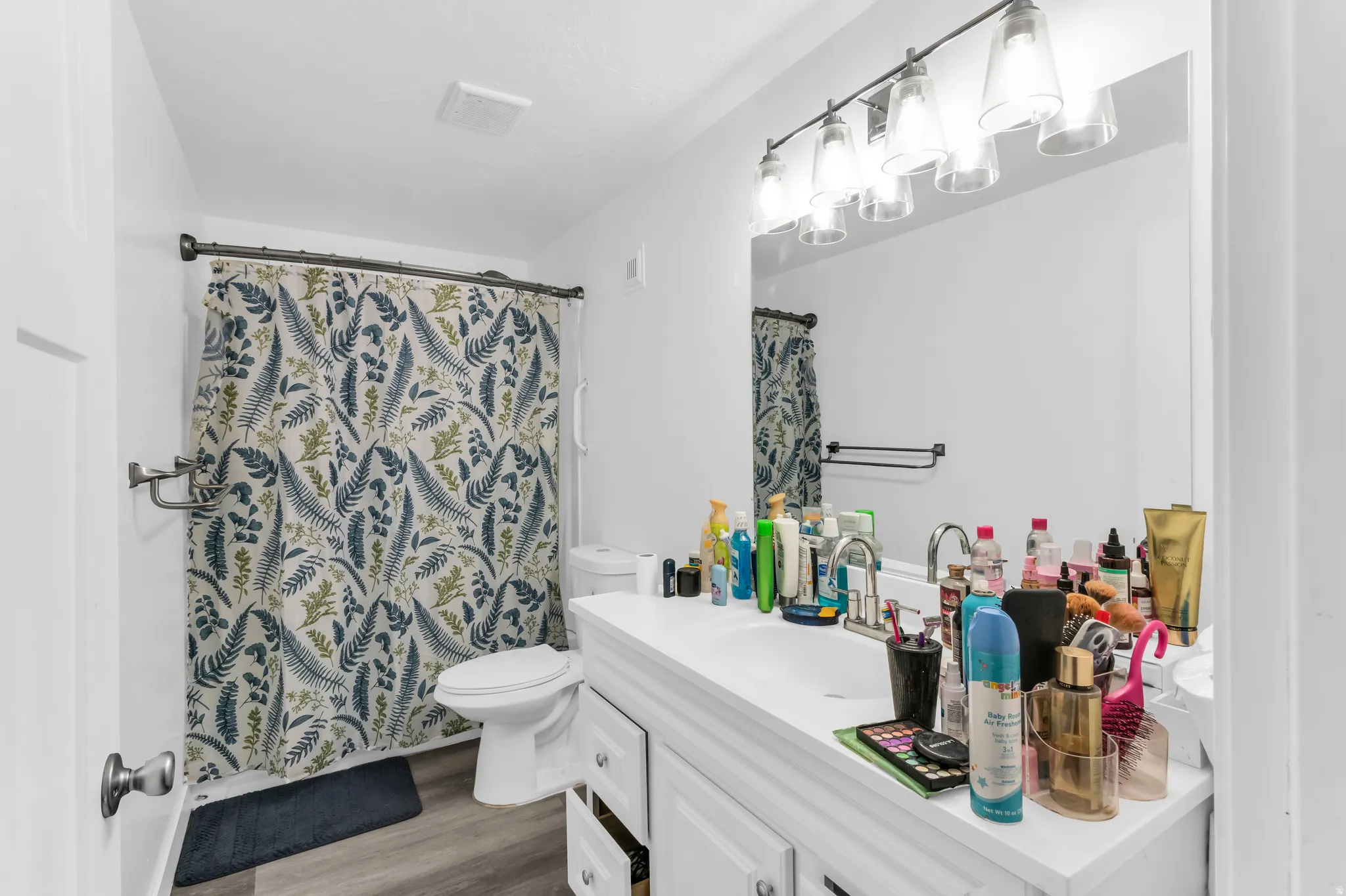 Bathroom with wood-finish flooring, white vanity with integrated sink, and a multi-bulb vanity light fixture