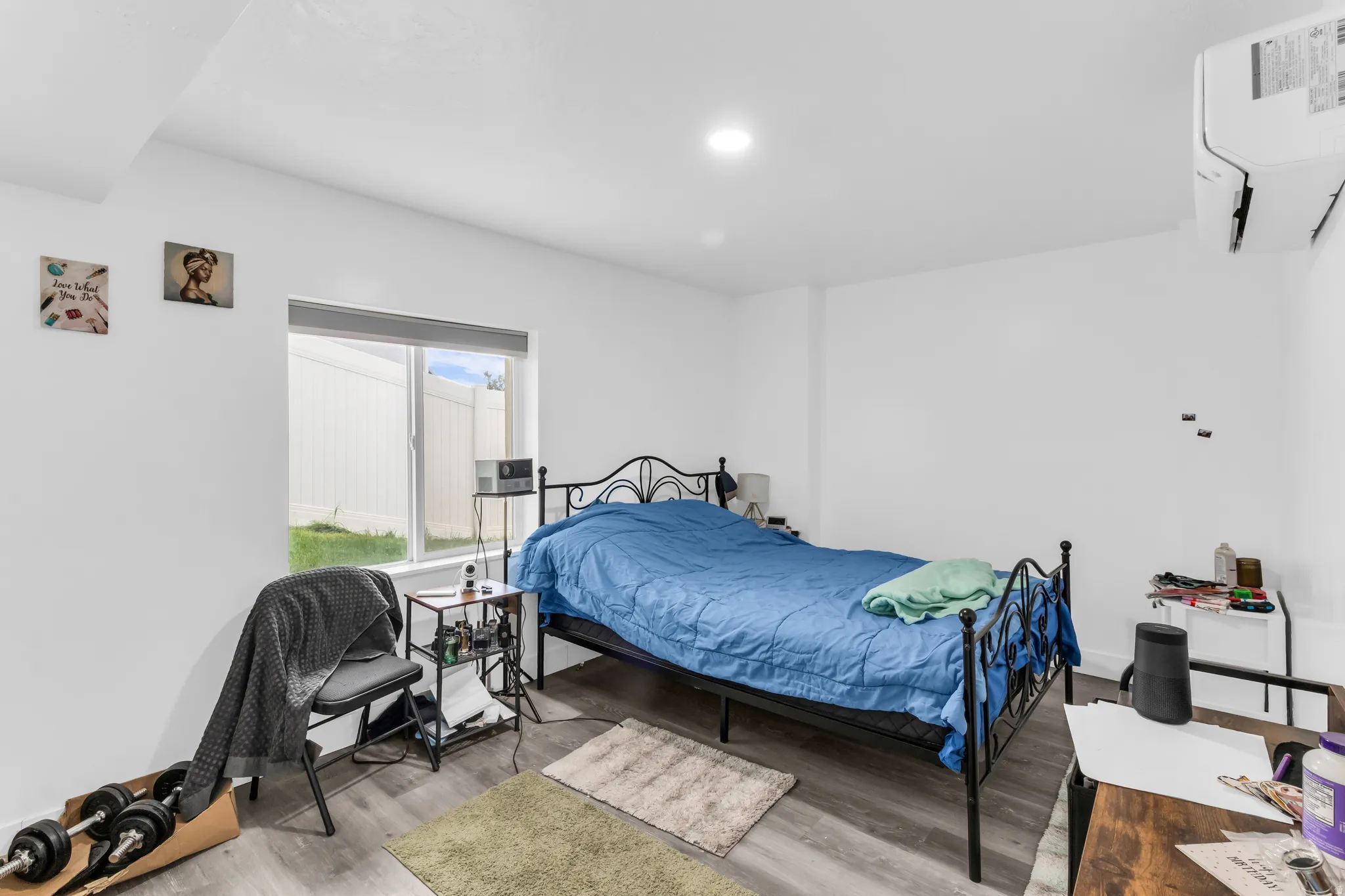 Recessed ceiling lighting, wood-finish flooring, white walls, and a window with a roller shade