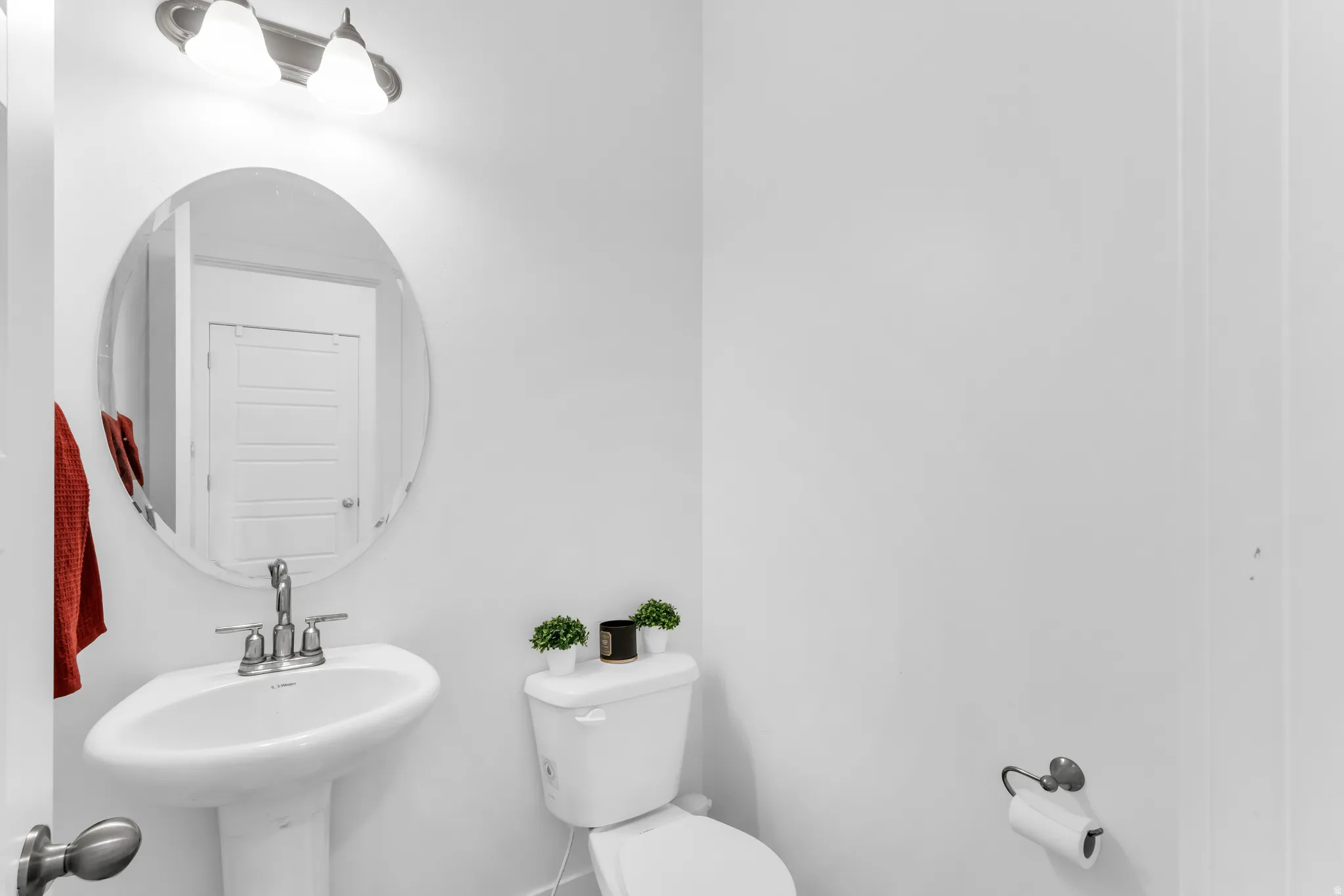 Pedestal sink with chrome faucet, oval wall-mounted mirror, and overhead vanity lighting