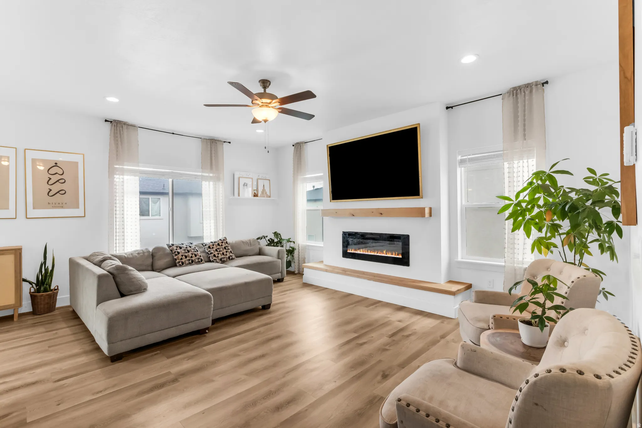 Living area featuring wood-finish flooring, recessed lighting, ceiling fan, an electric fireplace with a wood mantel, and multiple windows