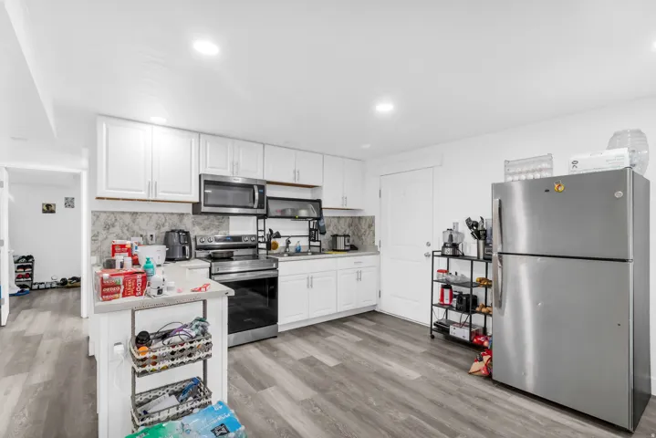 Kitchen featuring stainless steel appliances, white cabinetry, a patterned backsplash, and wood-finish flooring