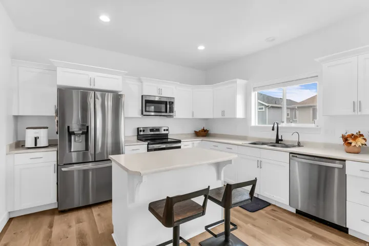 White cabinetry kitchen with stainless steel appliances, light-toned countertops, and wood-finish flooring