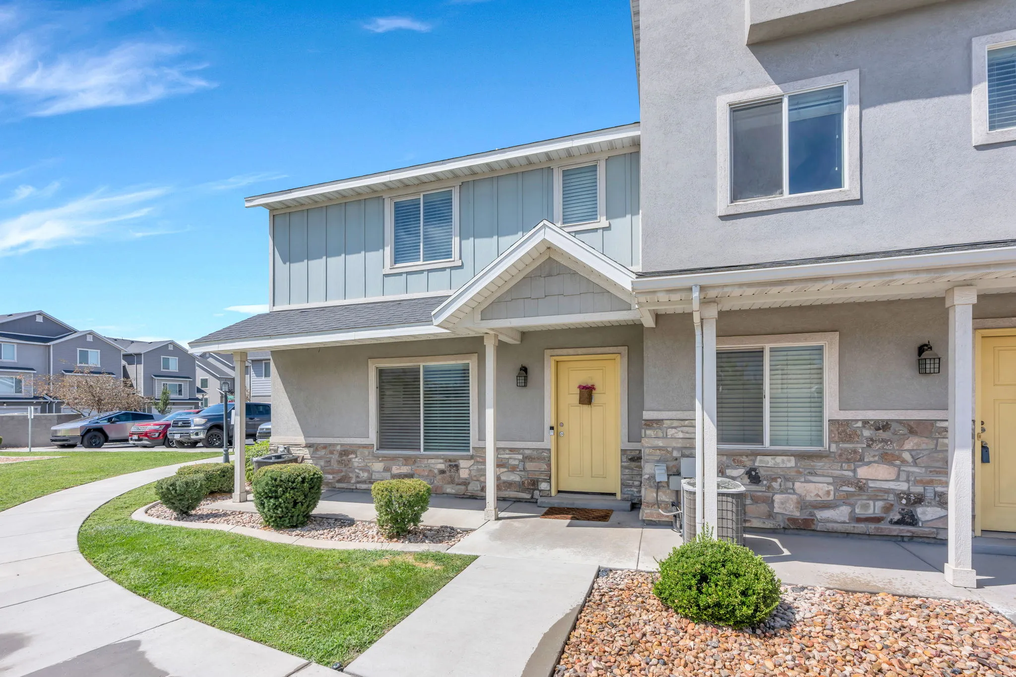 Exterior featuring a stone veneer and stucco finish, a covered porch entry, a light yellow front door, light blue vertical siding, and a concrete walkway