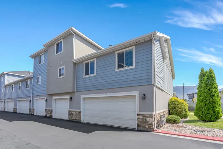 Multi-level townhouse with siding and stucco exterior, individual garages, and a stone veneer foundation