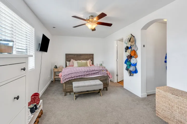 Carpeted room featuring a ceiling fan with integrated lighting, window with horizontal blinds, and a built-in archway opening
