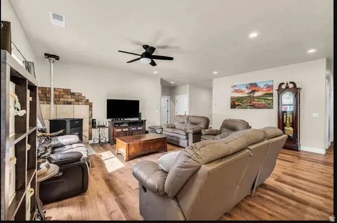 Vaulted ceilings, wood-finish flooring, recessed lighting, ceiling fan, and a fireplace with brick and tile surround
