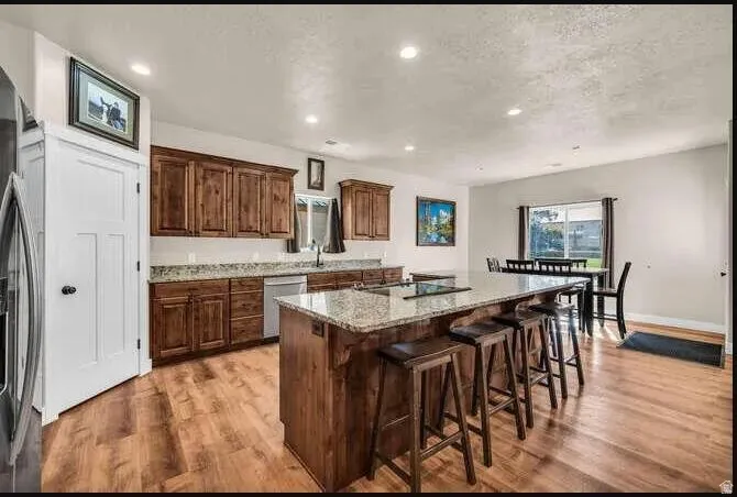 Open-concept kitchen with wood-finish flooring, recessed lighting, wood cabinetry, and a center island with a granite countertop