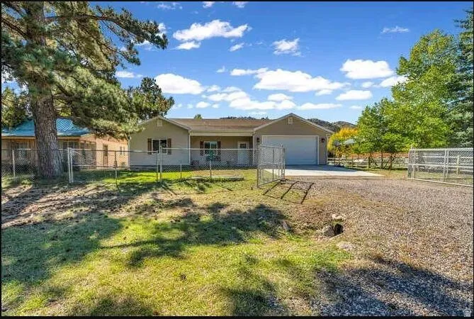 Single-story residence featuring a two-car garage, gravel driveway, and chain-link fencing