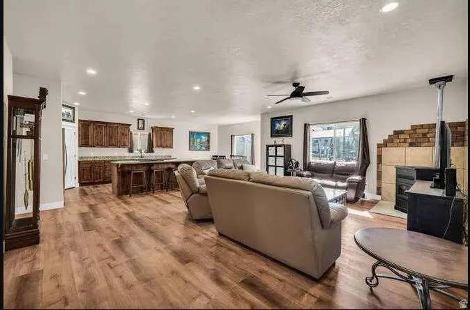 Open-concept living area with wood-finish flooring, a kitchen island with seating, dark wood cabinetry, a fireplace with a light-colored tile surround, and a ceiling fan