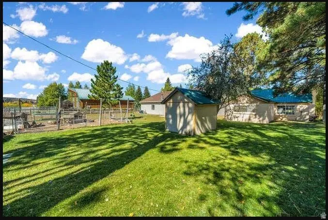 Expansive grassy yard with a detached storage shed, mature trees, and fencing