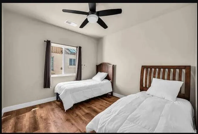 Vaulted ceiling, wood-finish flooring, ceiling fan, and a window with curtains