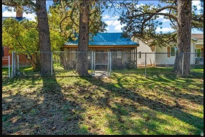 Chain-link fence with gate, established trees, and a house featuring a blue metal roof