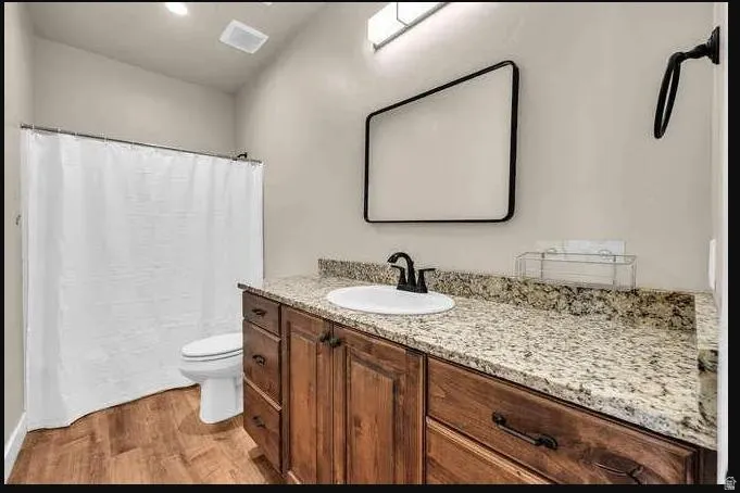 Wood-finish flooring, single vanity with wood cabinetry, light-toned countertop, and a white sink with a black faucet