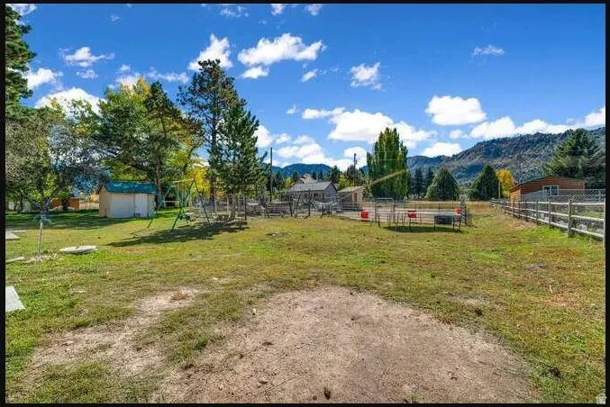 Expansive grassy area with mature trees, mountain backdrop, and partial fencing