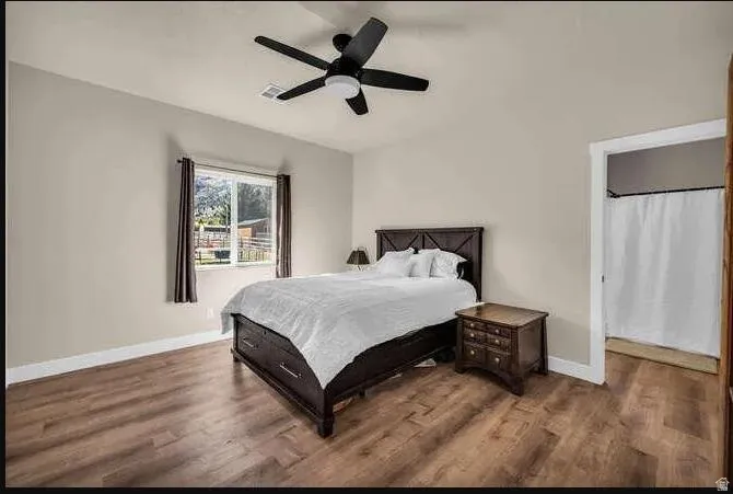 Neutral painted walls with wood-finish flooring, featuring a ceiling fan with integrated lighting, and a window with a backyard view