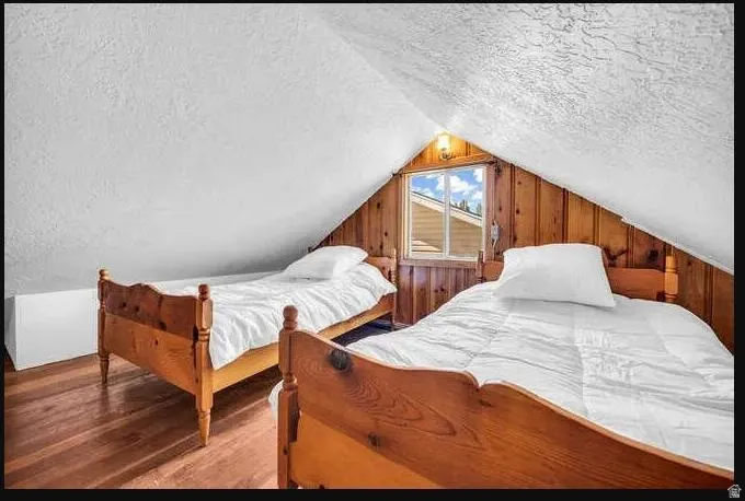 Attic space featuring wood-paneled walls, a window, wood-finish flooring, and sloped ceilings