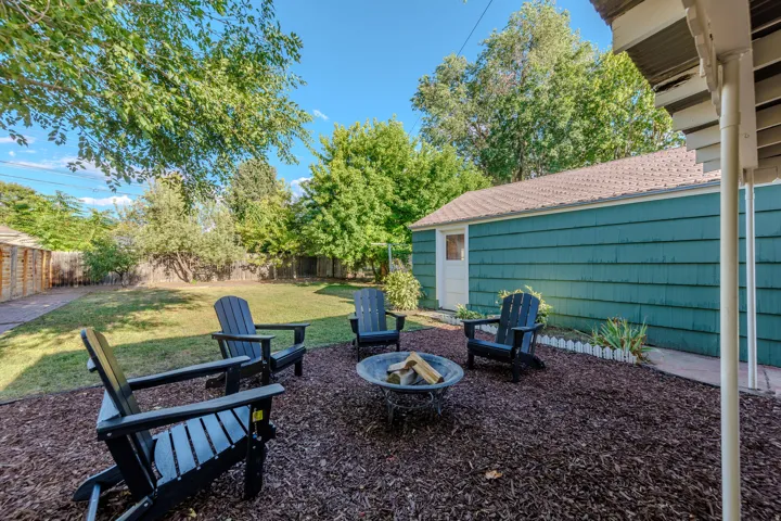 Private backyard featuring a fire pit area with mulch ground cover, a manicured lawn, and mature trees