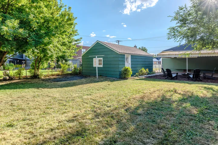 Detached outbuilding with siding exterior, covered patio, and mature trees